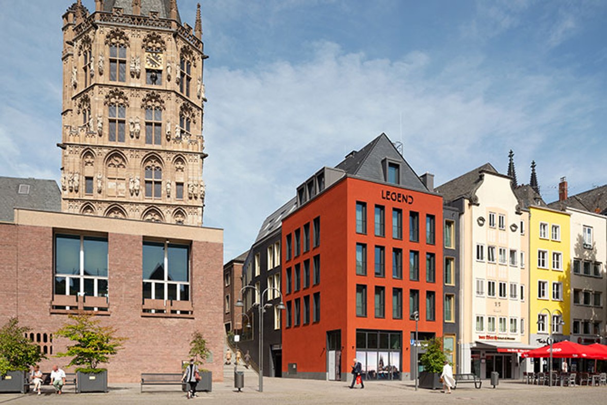 Ein signalrotes Haus am Alter Markt in Köln. Links daneben das Rathaus mit dem historischen Rathausturm